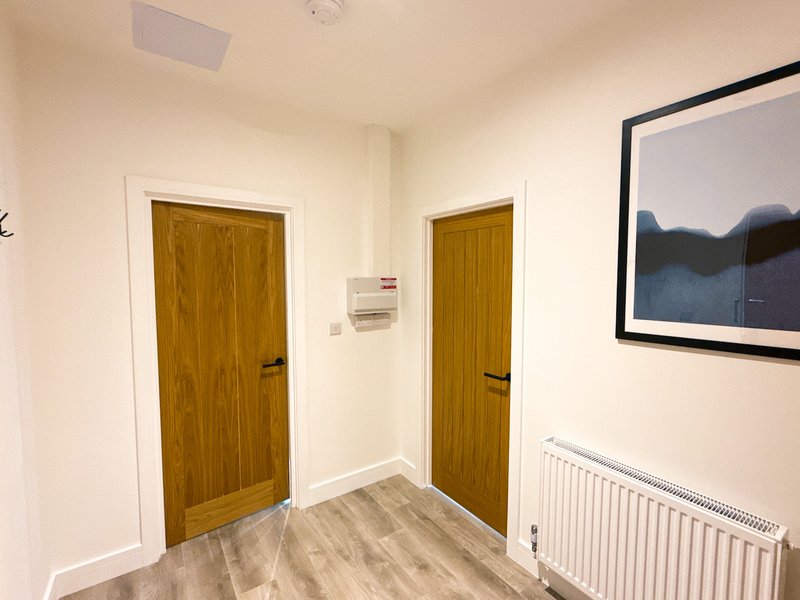 Hallway with two wooden doors, radiator, framed artwork and light wood flooring