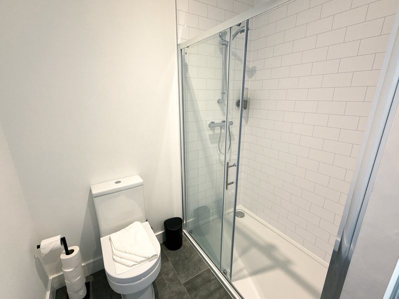 Modern bathroom with white subway tiles, glass shower enclosure, toilet and small black waste bin
