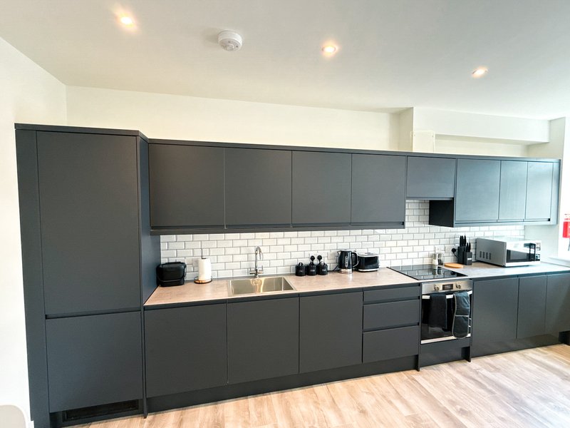 Modern kitchen with dark cabinetry, white subway tile backsplash, wooden countertop and integrated appliances