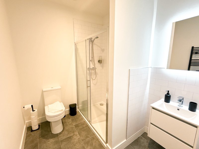 Modern bathroom with white tile, walk-in shower, toilet, and vanity sink with mirror