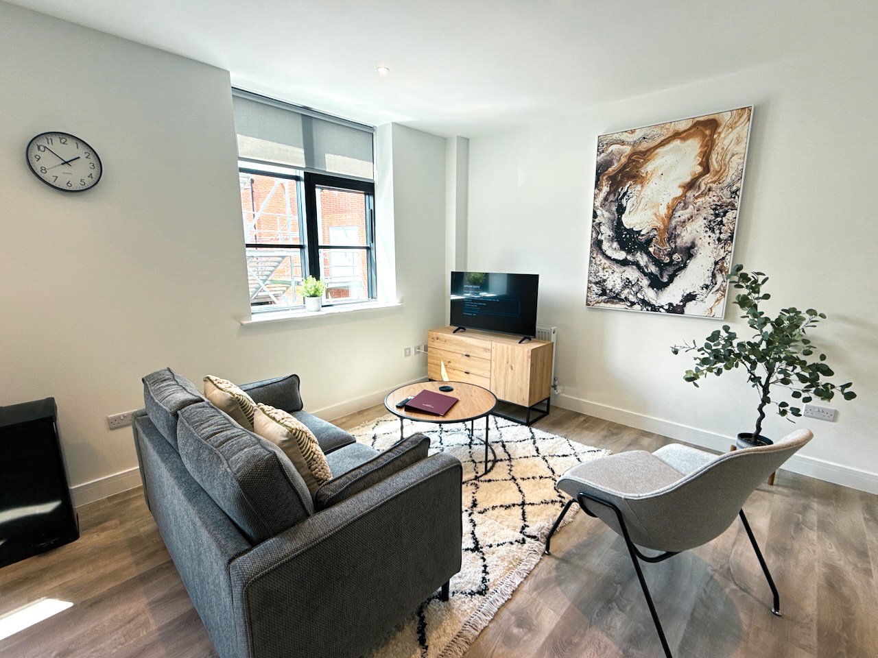 Bright living room with grey sofa, wooden TV unit, armchair, wall art and potted plant