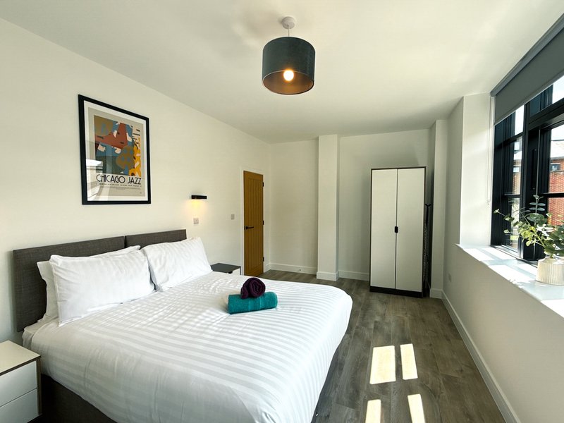 Modern bedroom with double bed, white bedding, black headboard, framed artwork and pendant light