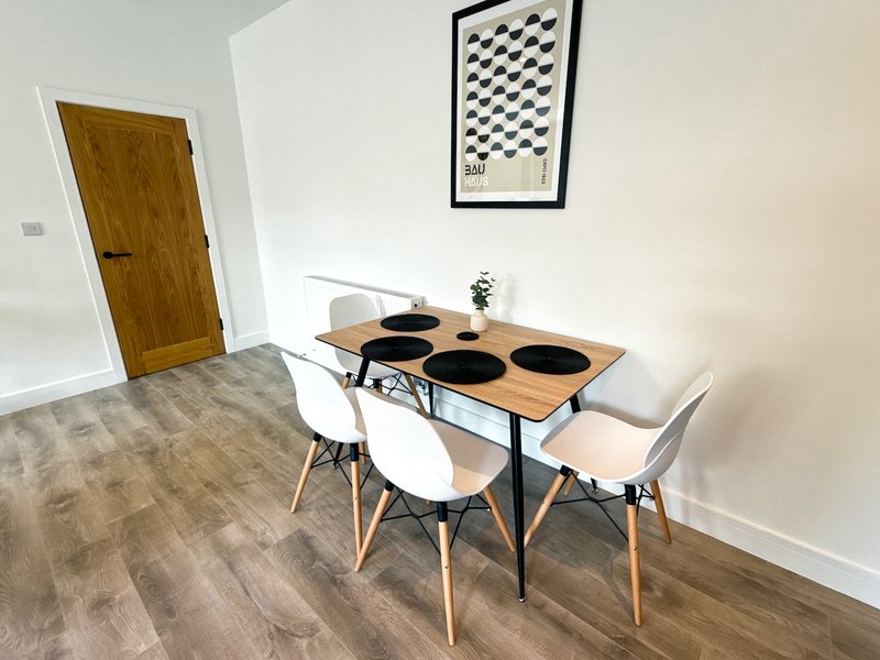 Dining area with wooden table, white chairs, and geometric wall art