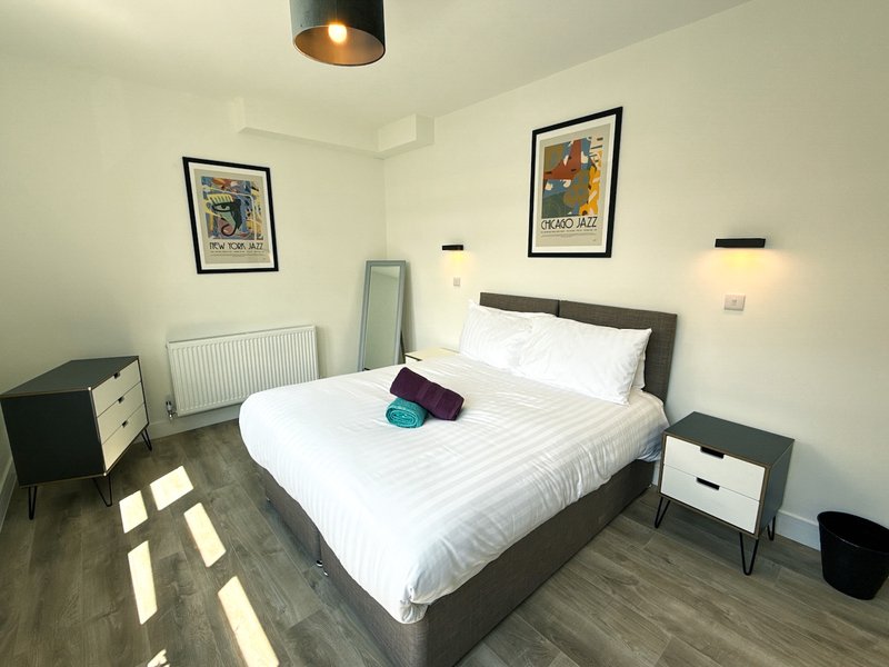 Modern bedroom with double bed, white bedding, wooden flooring, framed artwork and pendant lighting