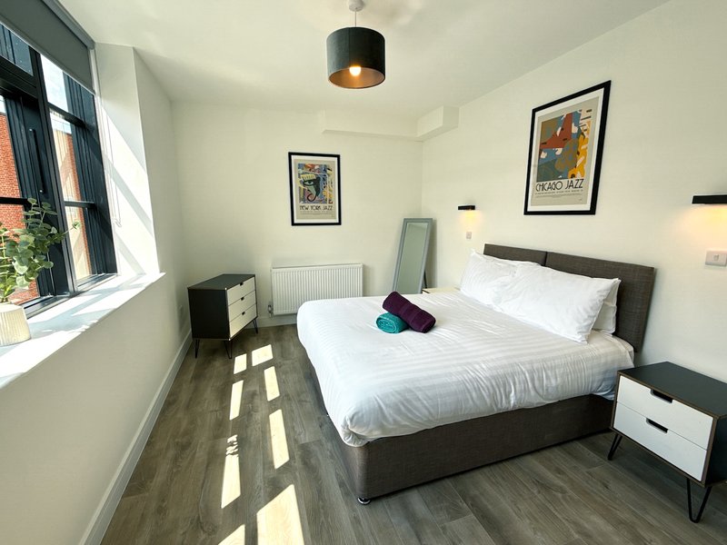 Modern bedroom with double bed, dark headboard, white bedding, wooden floor and framed wall art
