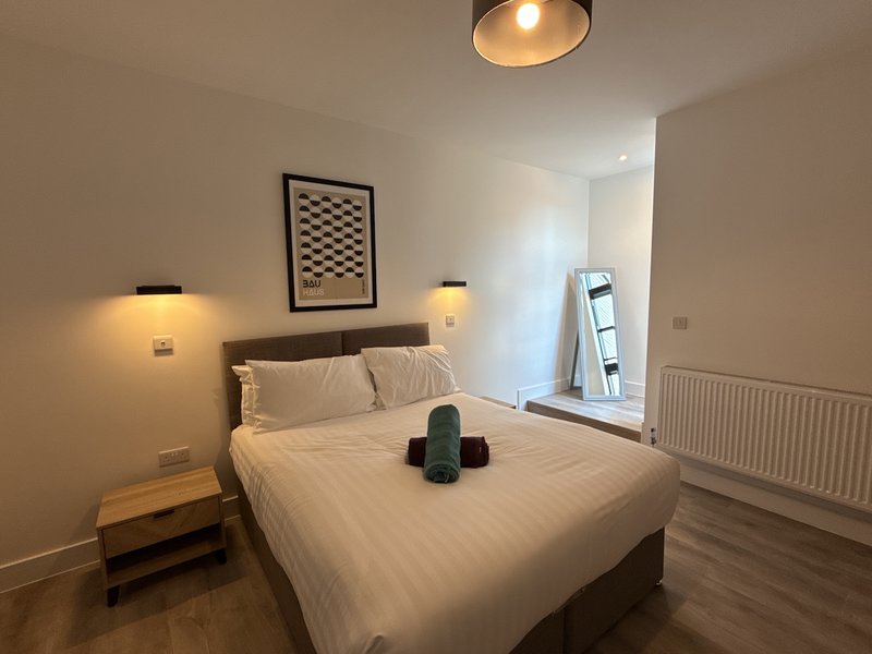 Modern bedroom with double bed, wall-mounted lights, framed artwork, and mirror