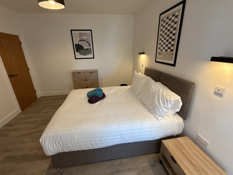 Modern bedroom with double bed, white bedding, gray headboard, wooden nightstands, and wall art