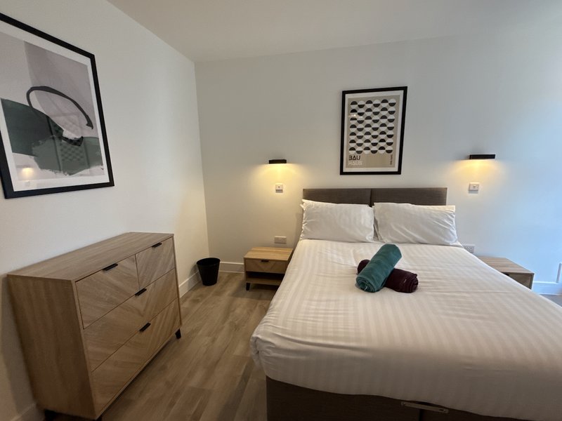 Modern bedroom with double bed, wooden dresser, wall art, and bedside lighting