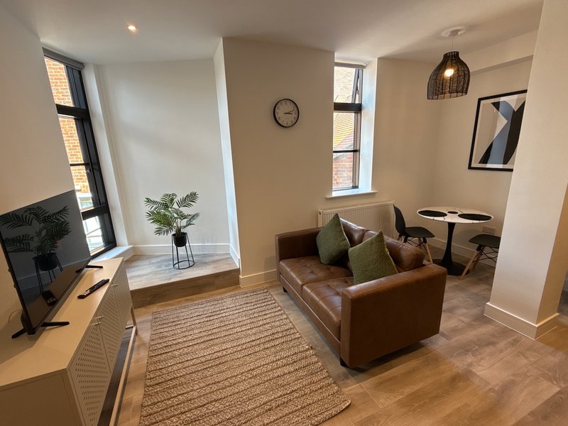Modern living room with brown leather sofa, wooden desk, TV, and large windows