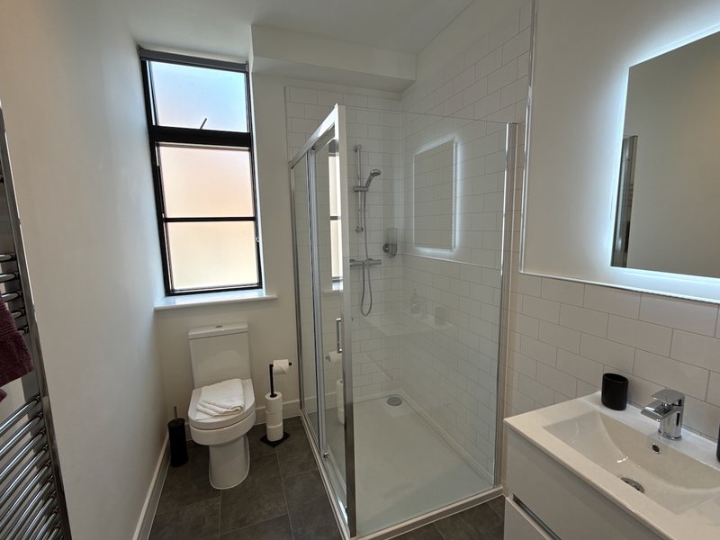 Modern bathroom with toilet, enclosed shower, sink and illuminated mirror