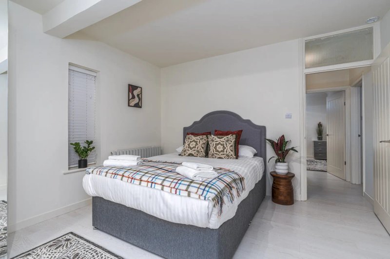 Modern bedroom with grey upholstered bed, plaid bedding, decorative pillows and potted plants