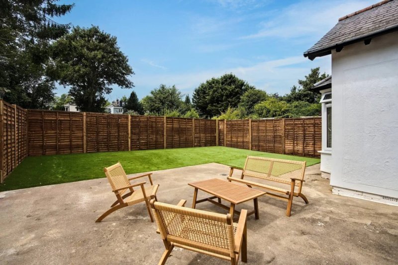 Back garden with patio, wooden furniture, lawn, fence and adjacent house