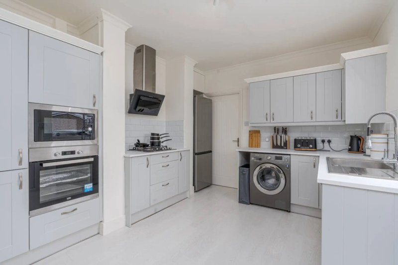 Modern white kitchen with integrated appliances, washing machine, and stainless steel fixtures