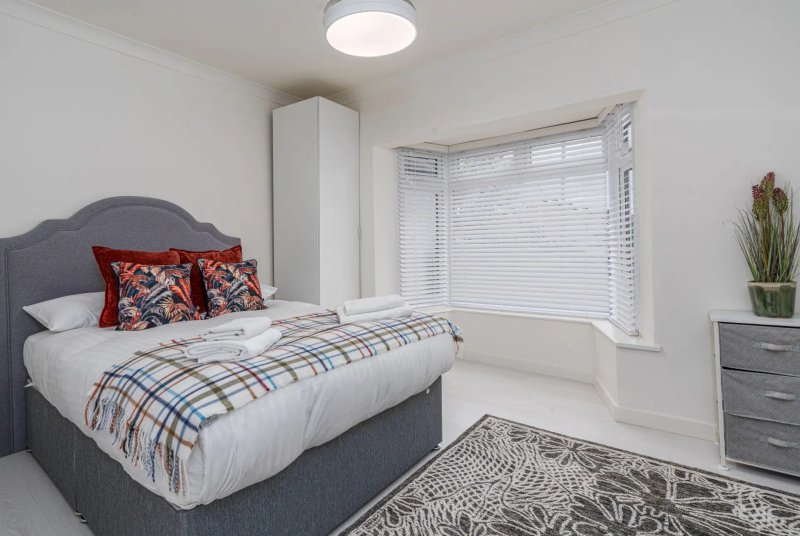 Bright modern bedroom with double bed, grey upholstered headboard, patterned bedding, and large window