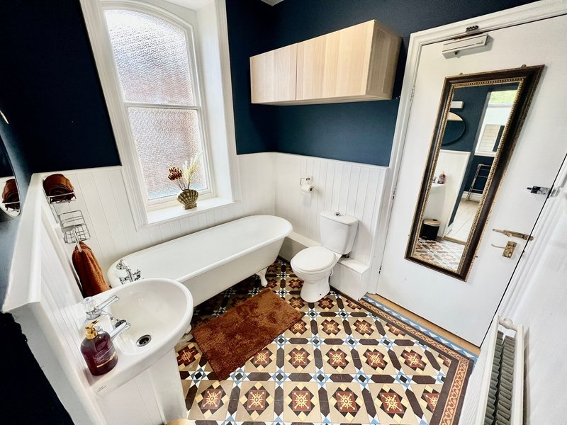 Modern bathroom with dual sinks, bathtub, toilet, patterned floor tiles and dark blue walls
