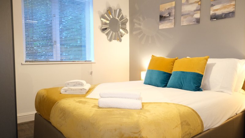 Bedroom with double bed, yellow bedding, colorful pillows, and window with blinds