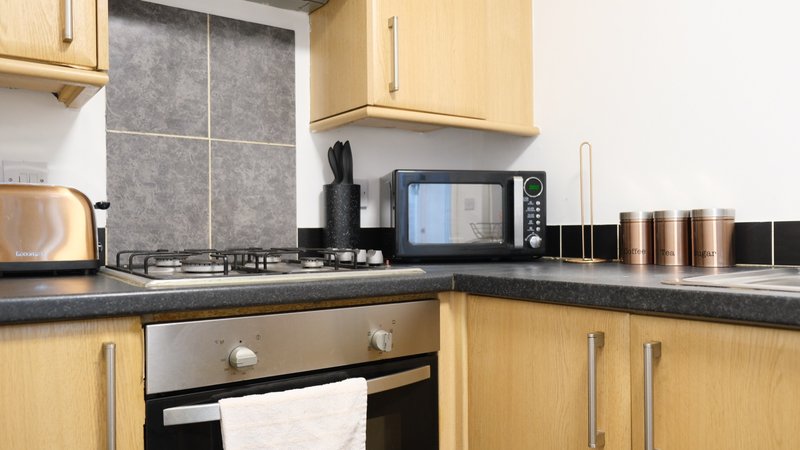Modern kitchen with light wood cabinets, black countertop, built-in oven and microwave