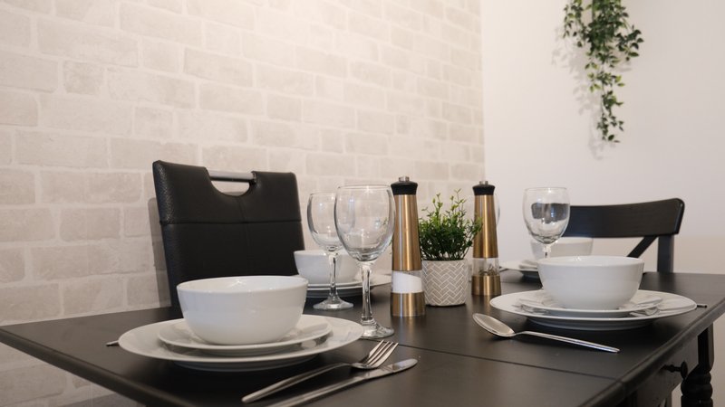 Dining table set for two with white bowls, plates, glasses and black chairs