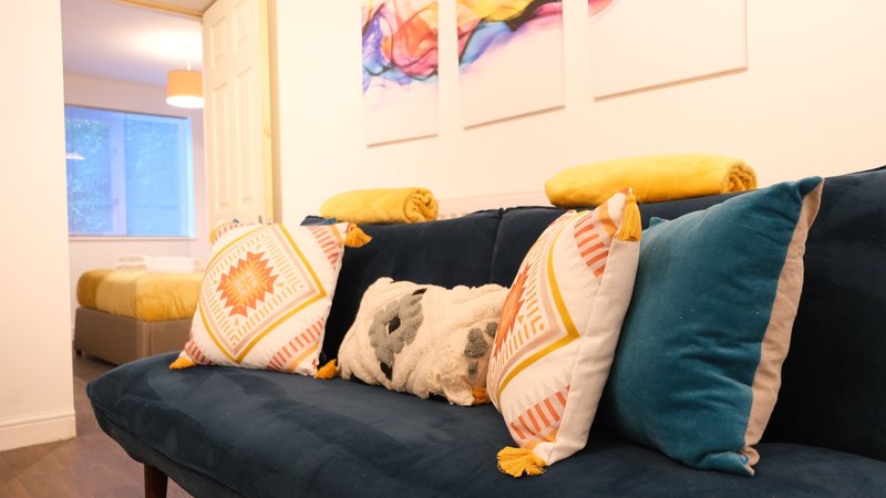 Living room with dark sofa, colorful cushions, wall art, and window with blue evening light
