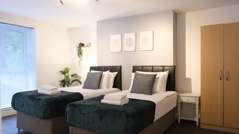 Modern bedroom with two single beds, dark headboards, patterned cushions and wardrobe