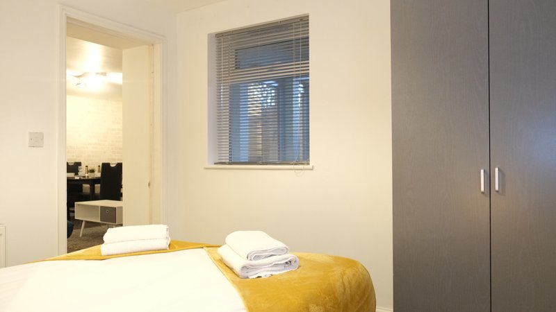 Bedroom with double bed, yellow throw, wardrobe and window with blinds