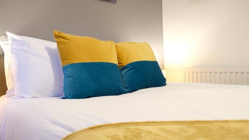 Bedroom with white sheets, colorful yellow and blue cushions, and radiator
