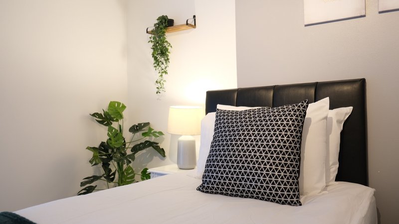 Modern bedroom with black headboard, patterned cushion, white bedding, potted plants and wall-mounted greenery