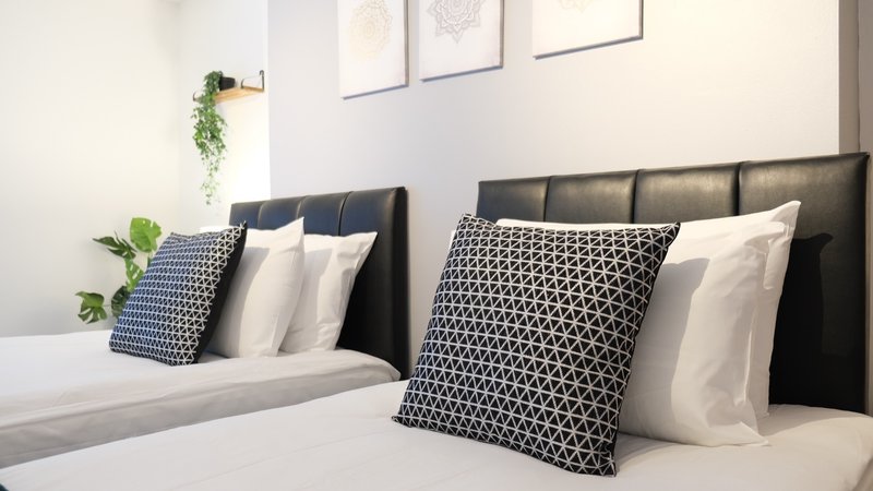 Modern bedroom with two black upholstered beds, patterned pillows, white bedding and wall art