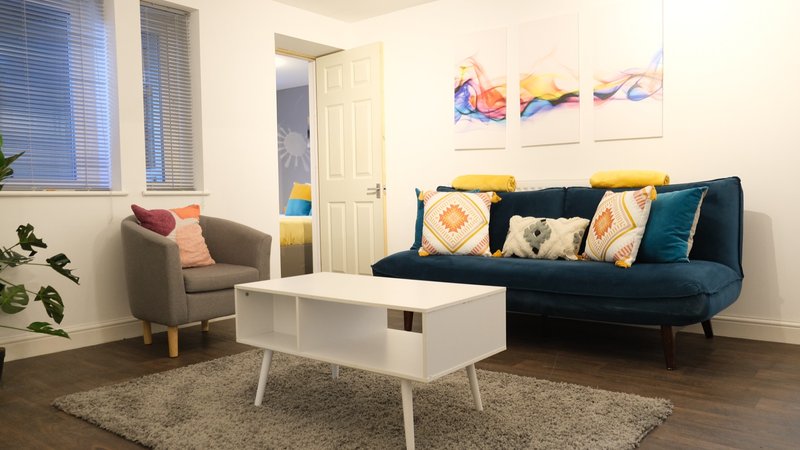 Modern living room with dark blue sofa, grey armchair, white coffee table and colourful wall art