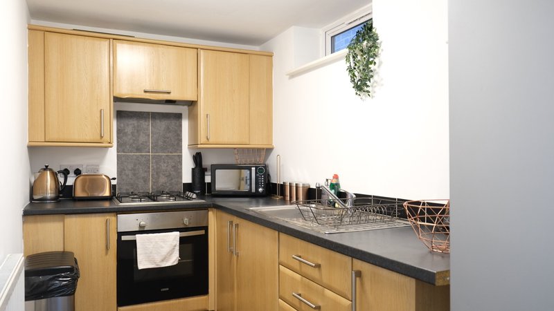 Compact kitchen with wooden cabinets, black countertop, integrated oven and hob