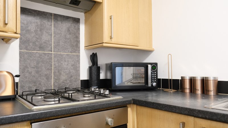 Kitchen with gas hob, microwave, kettle and copper canisters on black countertop