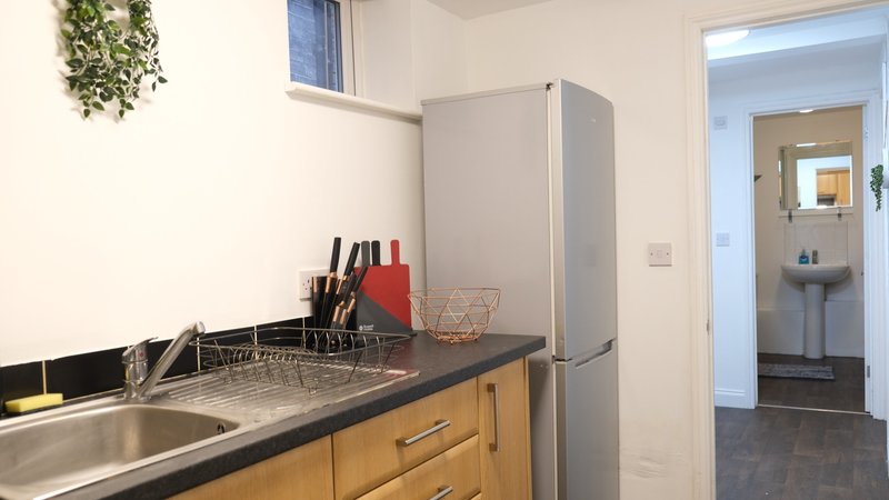 Kitchen with wooden cabinets, stainless steel sink, grey fridge and open doorway to bathroom