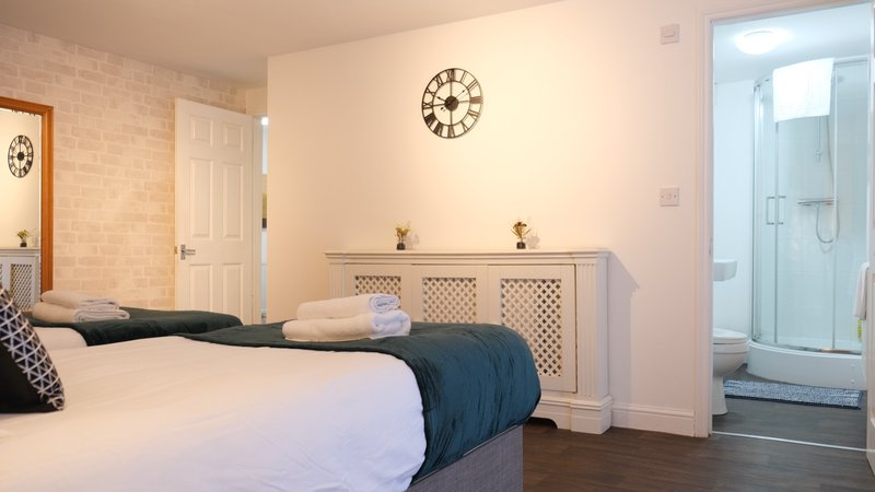 Bright bedroom with double bed, white dresser, wall clocks, and ensuite bathroom visible