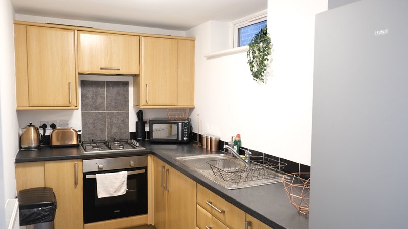 Compact kitchen with wooden cabinets, black countertop, integrated oven and sink