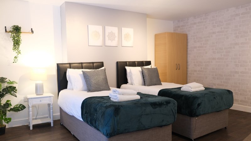 Twin bedroom with dark headboards, white bedding, rolled towels, wooden wardrobe and wall art