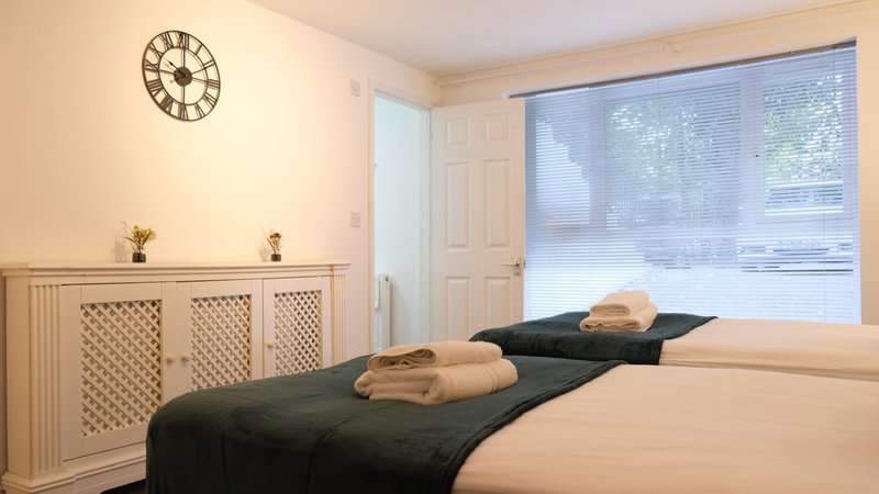 Bright bedroom with two beds, wall clock, storage cabinet and large window