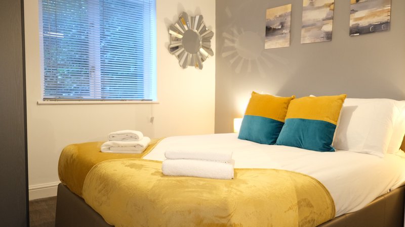 Bedroom with double bed, yellow bedding, colorful cushions, and wall-mounted clock