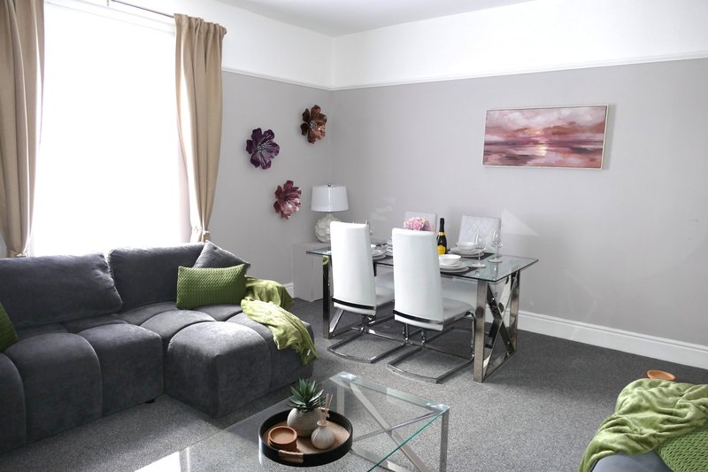 Modern living room with gray sectional sofa, glass desk, white appliances and floral wall art