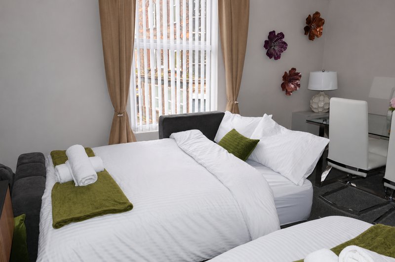 Modern bedroom with white bedding, green cushions, wall flowers and vertical blinds.