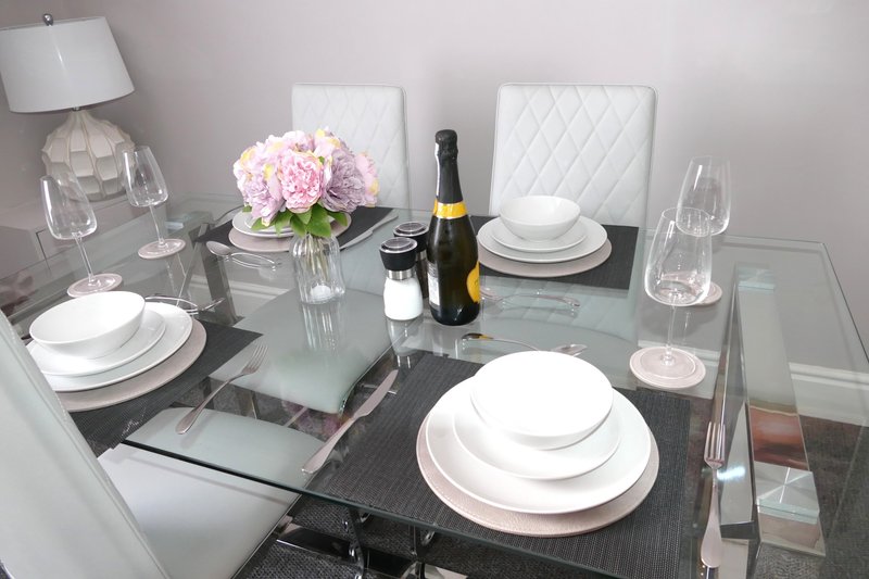 Dining table set with white plates, glasses, wine bottle, and pink flowers in vase