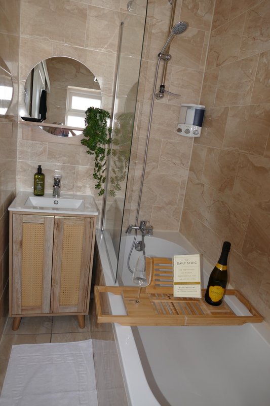 Modern bathroom with tiled walls, vanity unit, mirror, shower enclosure and wooden bath tray.