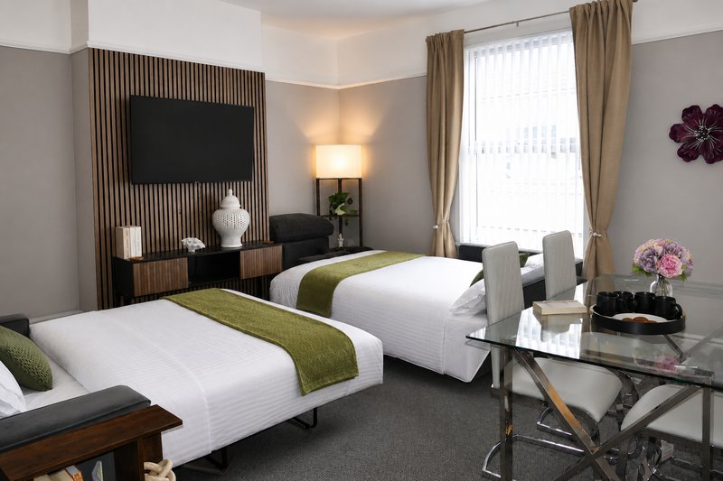Modern twin bedroom with two beds, desk, TV wall, and large windows with curtains