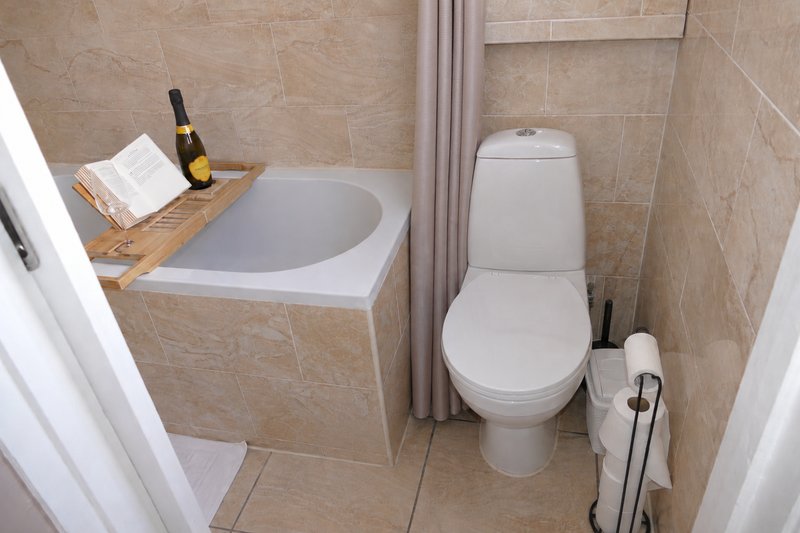 Compact bathroom with soaking tub, toilet, beige tile walls and wooden shelf.