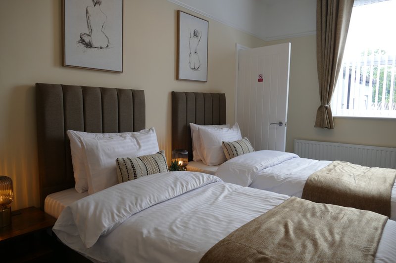 Bedroom with two double beds, brown upholstered headboards, white bedding, framed artwork, and window with curtains.