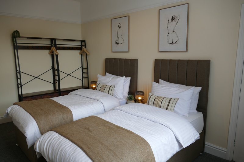 Twin bedroom with two beds, grey upholstered headboards, white bedding and framed wall art