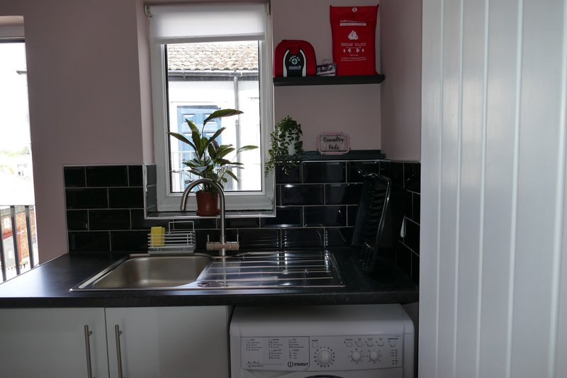 Kitchen with black tile backsplash, stainless steel sink, potted plant, and window above counter