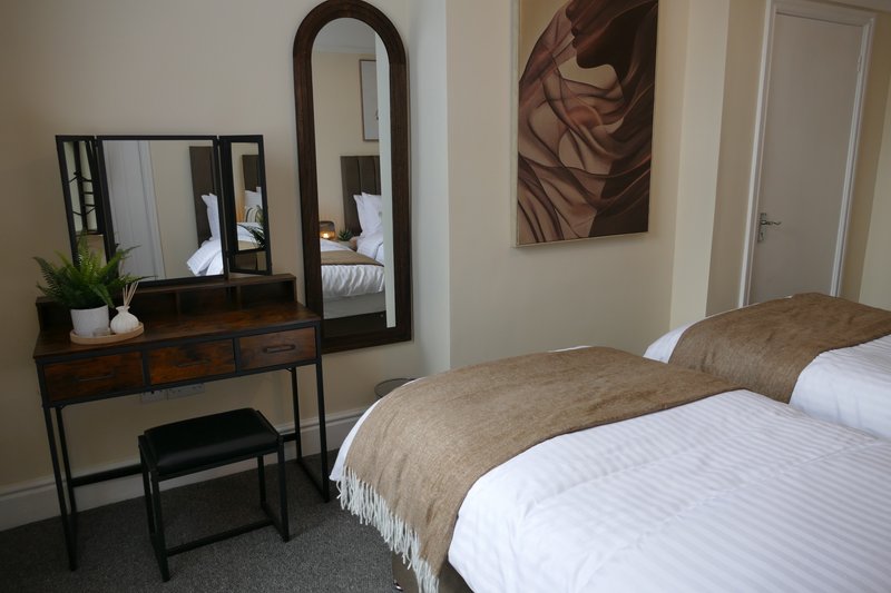 Bedroom with two beds, wooden vanity mirror, wall art, and grey carpet flooring