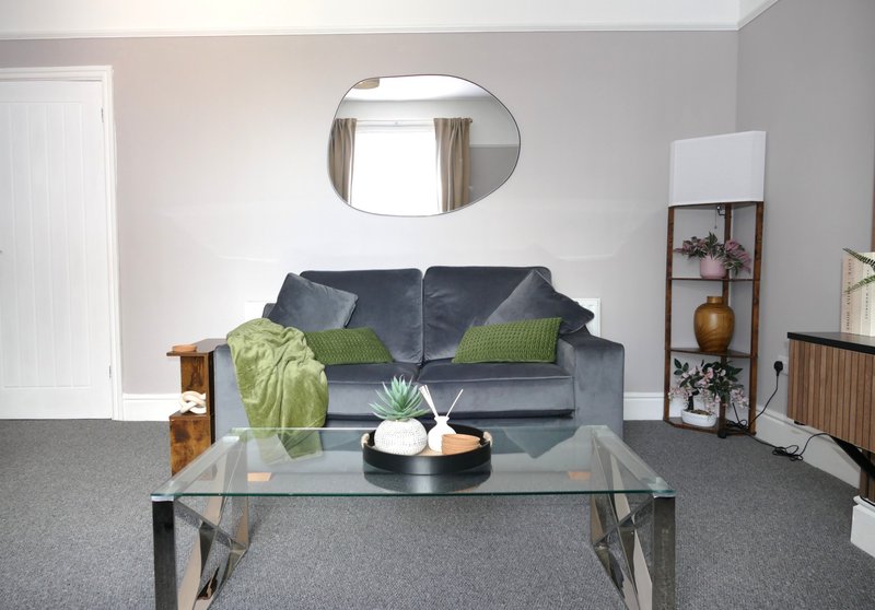 Living room with gray sofa, glass coffee table, oval mirror and decorative shelving unit