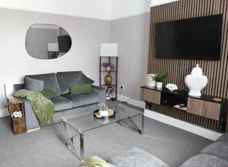Modern living room with gray sofa bed, glass coffee table, wall-mounted TV, and decorative accessories