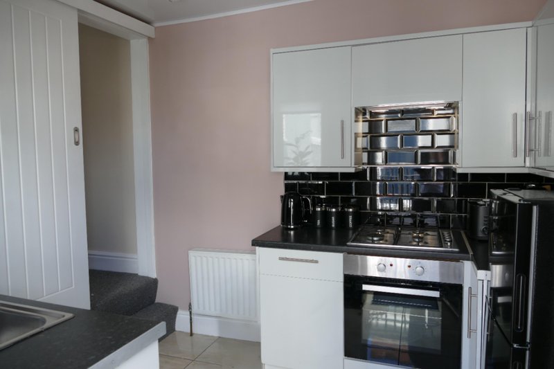 Modern kitchen with white cabinetry, black splashback, built-in oven and shelving above